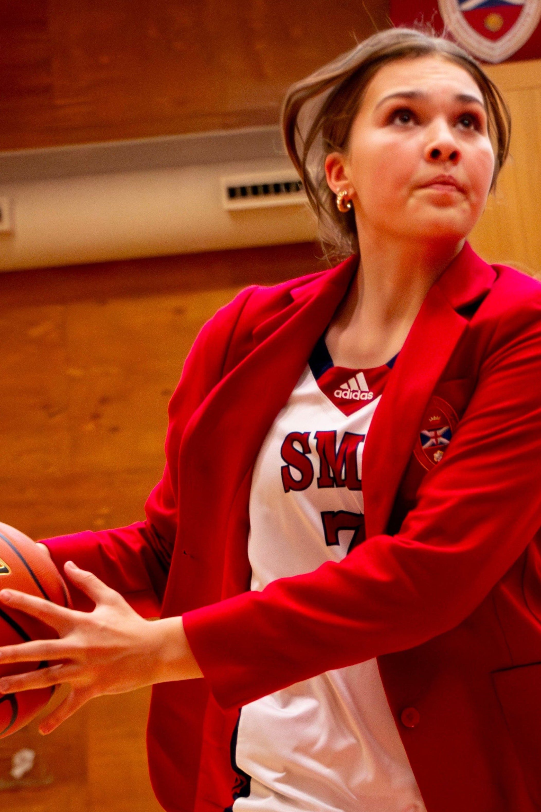 Person in red jacket holding a basketball on a gymnasium floor.